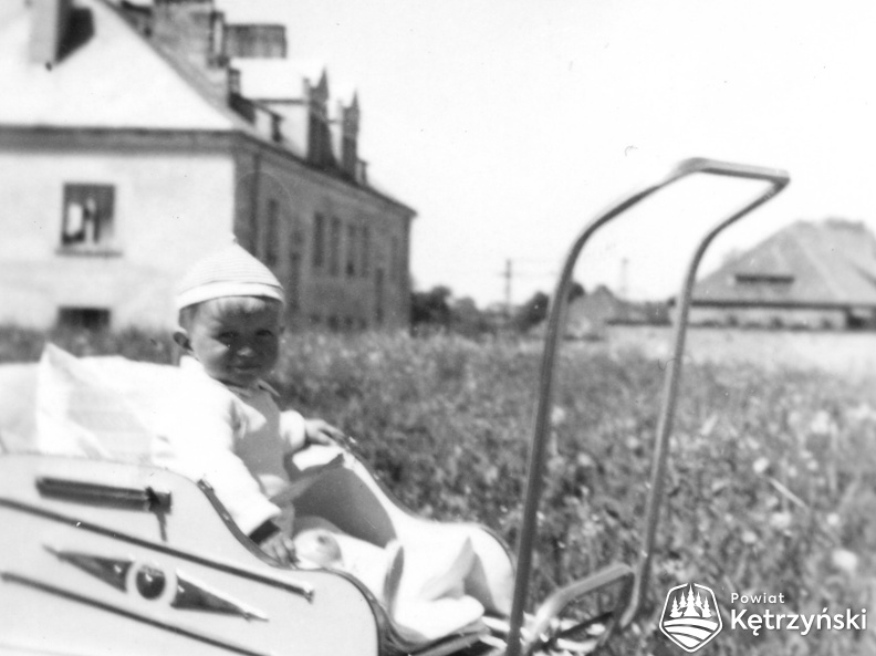 Edward Kamiński w wózeczku na tle domu pracowników cukrowni przy ul. Ogrodowej 1958r.